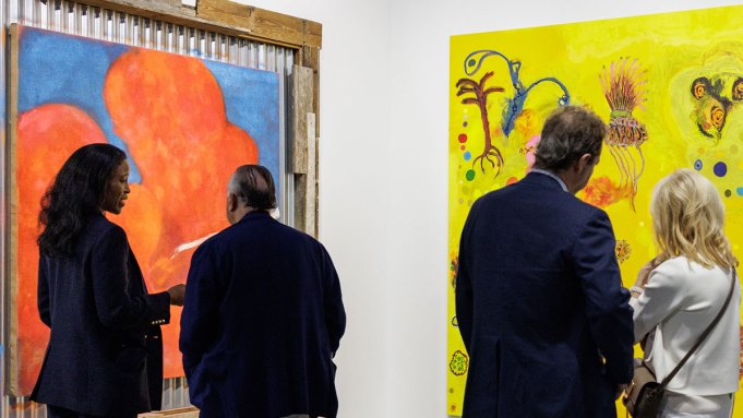 Four people look at two paintings in an art fair booth.
