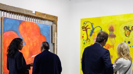 Four people look at two paintings in an art fair booth.