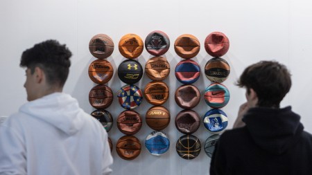 Two people standing in front of a sculpture featuring rows of deflated basketballs.