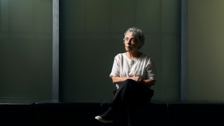 A woman sitting in a darkened space with her legs crossed.