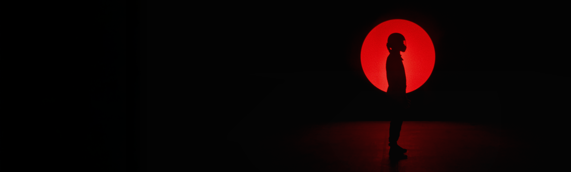 A silhouette of a person standing in profile against a black background. Behind the figure, a large glowing red circle creates a strong visual contrast.